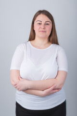 Beautiful chubby girl in 30s posing in studio wearing casual white t-shirt with crossed hands,looking in camera.Pretty young plus size woman pose with smile.Attractive Caucasian female model portrait