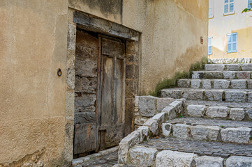 The village of Mons in the country of Calian. Medieval village in the South of France. Stone staircase in a sloping street. A picturesque wooden door in a corner of the staircase.