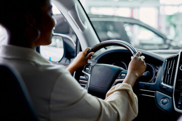 rear view on young african woman sitting behind the wheel of automobile in cars showroom