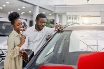 young and beautiful married couple in cars showroom, confident black man buy new car as a present for his wife