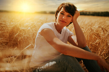 portrait of a woman sitting in a wheat field under a sunset