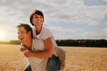 a woman on the back of a man having fun in a wheat field