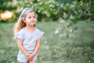 A charming little girl with long blond hair playing against the background of nature. A happy child enjoys summer time in the Park.