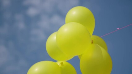 Woman's hand holding yellow balloons against the blue summer sky. Fiesta - Powered by Adobe