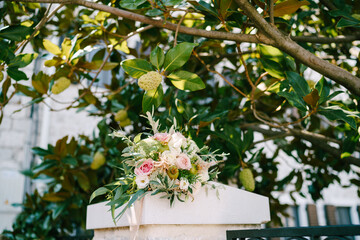 bridal bouquet of white and pink roses, branches of eucalypt tree, astilbe, ammi, small green pomegranates and pink ribbons on the fence under magnolia tree