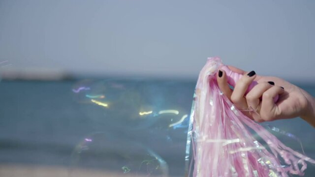 Close up of a girl's hand holding a cheerleader pompom by the beach. Summer breeze and soap bubbles