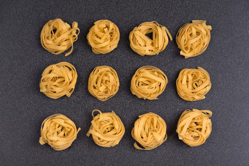 Fettuccine Tagliatelle pasta on grey background. Spaghetti nests. Uncooked ingredient for traditional Italian cuisine