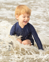 Young boy, four years old, running and playing at the beach. Blonde hair and navy swimming suit, smiling and laughing.