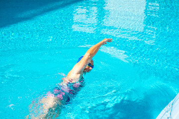Senior woman practicing swim in the outdoor swimming pool, wearing goggles and swimming cap, active and healthy lifestyle in retirement