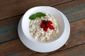 fresh diet curd homemade in a white plate with ripe strawberries and mint leaf on wooden background from boards. healthy breakfast option