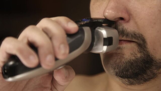 a man shaves his stubble. the guy cleans his beard with an electric razor. morning treatments in the bathroom. half of the beard close-up. copy space