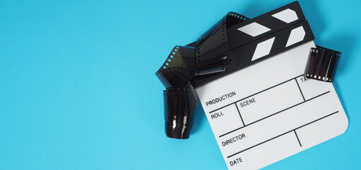 Small white clapper board and film roll on blue or turquoise background. It use in movie and video production.