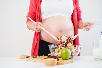 Obraz na płótnie Canvas Pregnant young asian woman eating fruit salad fresh, Fruit salad is healthy food for baby or fetus. Pregnant mother hold blow of fruit salad. Pregnancy, health care concept White backdrop