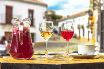 Pitcher of sangria with coffee cup and red and white glasses of wine on a blurred Spanish countryside background in Spain.