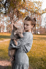 Beautiful red-haired girl with a fox in her arms against the background of the forest, animal rescue, domestication of wildlife, a woman with an original hairstyle