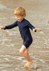 Young boy, four years old, running and playing at the beach. Blonde hair and navy swimming suit, smiling and laughing.