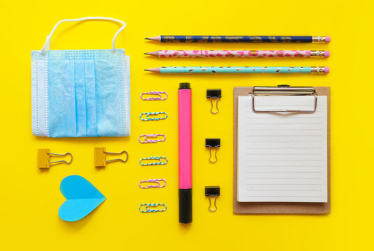 School supplies flatlay on yellow background. Clip board, paper clips, notebook, marker, paper heart, pen, clamp, fase mask. Back to school 2020. Online education. School banner. Geometric composition