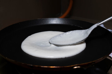 spreading dosa or idli batter on non stick tawa with spoon for making delicious round dosa