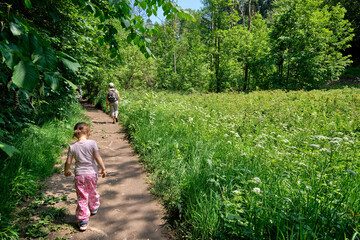 Rear view of mother hiking with her daughter on a natural footpath in an idyllic green forest to...