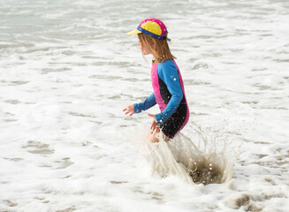 Young girl, 6 years old, in a brightly colored swimming suit, running and playing at the beach