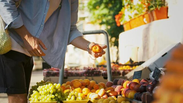 Unknown guy in casual clothes, string bag. Choosing nectarines at small street market with vegetables and fruits. Zero waste. Slow motion, close up