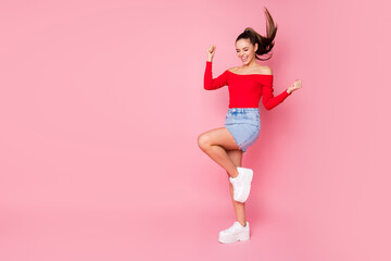 Full size photo of pretty crazy lady raise leg fists celebrating summer vacation beginning wear red open shoulders shirt mini denim skirt footwear isolated pastel pink color background