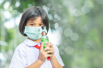 asian little school girl wearing mask holding alcohol sanitizer hand gel   during corona virus and flu outbreak. kid in School uniform going back to school after covid-19 quarantine and lockdown.