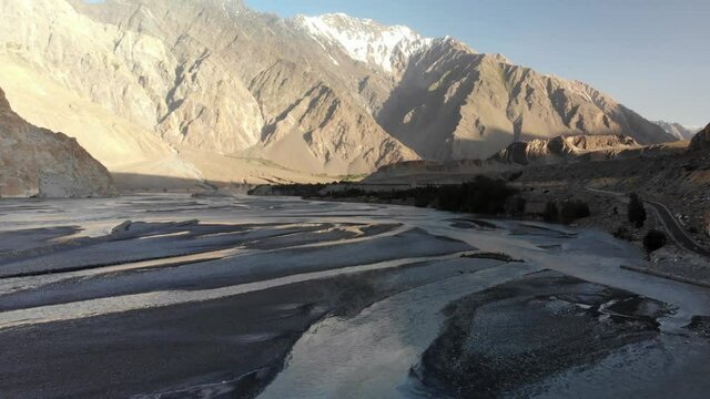 Forward-moving view of the Hunza valley with its the dry river, with arid mountains and snowy peaks in the background and a beautiful blue sky, Gilgit Baltistan region, Pakistan 