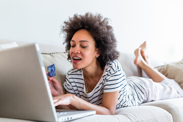 Internet payment. Happy cheerful woman looking at the Internet screen while making an Internet payment. Happy young woman with credit card and laptop sitting on sofa at home. Online payment