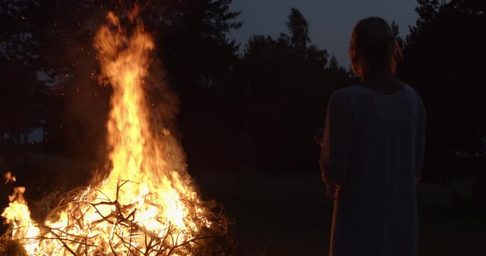 Natural woman wearing dress looking at bonfire at midsummer night