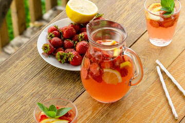 Summer pink lemonade with strawberries and lemon in a glass jug