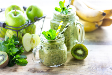 Two healthy green smoothies with spinach, banana, apple, kiwi and mint in glass jar and ingredients. Detox, diet, healthy, vegetarian food concept.