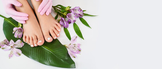 Obraz na płótnie Canvas Beautiful perfect female skin legs feet top view with tropical flowers and green palm leaf. Nail polish, care and clean, spa pedicure treatment in white. Concept on background isolated. Copy space