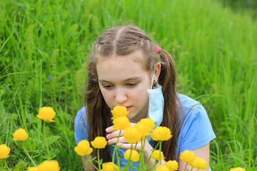 Happy cute teenager girl with long hair taking off face medical mask and sniffing flowers. Concept of the end of covid-19, coronavirus pandemic, allergy, seasonal allergic rhinitis, mask mode.