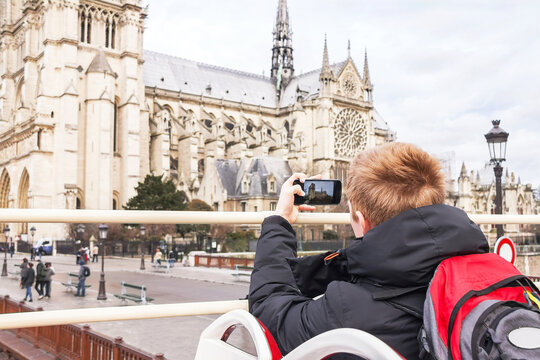 Teenager tourist is taking photo on cathedral of Notre Dame de Paris with mobile smart phone camera.