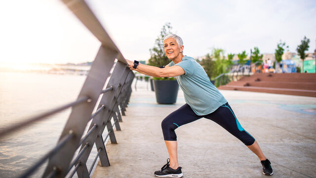 Smiling retired woman stretching legs outdoors. Senior woman enjoying daily routine warming up before running at morning. Sporty lady doing leg stretches before workout