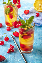 A refreshing summer drink with strawberries, cherries, currants and lemon in glasses on a table