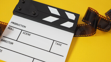 Small white clapper board and film roll on yellow background. It use in movie and video production.
