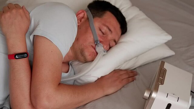 Close-up of healthy young adult man wearing under the nose nasal mask ( CPAP mask ) and using CPAP machine for sleeping smooth without snoring.