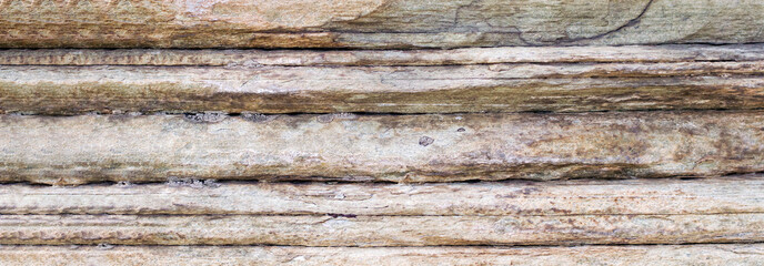 Relief of large gray rock, multi-storey layered rough sedimentary rocks. Natural big stone background, close up texture of layers of horizontal stone surface. Banner with copy space.