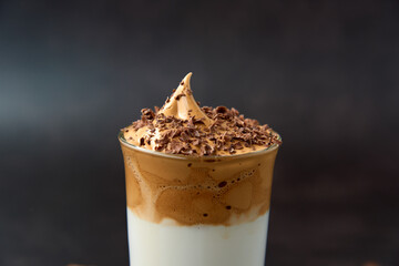 Close up of glass of trendy fluffy creamy dalgona or whipped instant coffee with milk and chocolate on the dark background. New popular food and drink trend concept. Copy space.