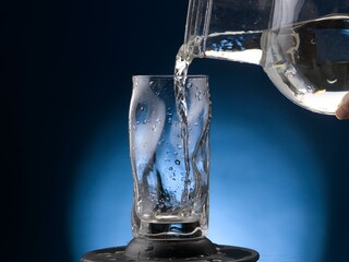 Pouring water into pint glass. Close-up on blue-black background