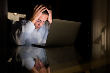 one teenager or millennial working or studying at late night for school or work - man tired of using his laptop after all day at home indoors lifestyle concept