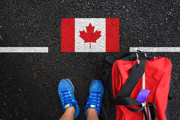 a man with a shoes and travel bag is standing on asphalt next to flag of Canada and border