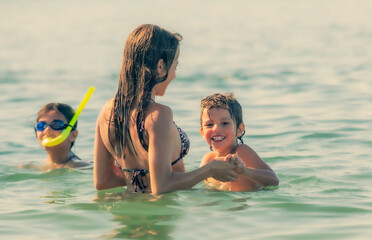 happy kids playing on the beach at the day time. Vacation activities. Little boy is learning to swim. Family together.