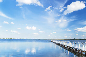 Blue sky with light clouds, blue water and white pier in the sunny summer day.