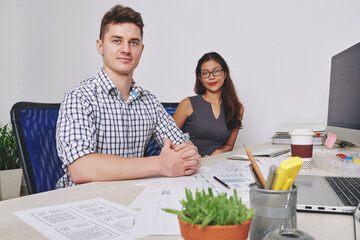 Team of positive confident young ux designers working on project at office desk