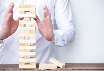 a man in a white shirt holds the tower with his hands so that it does not fall