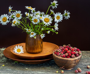 Sweet forest strawberries and a bouquet of daisies on a wooden background