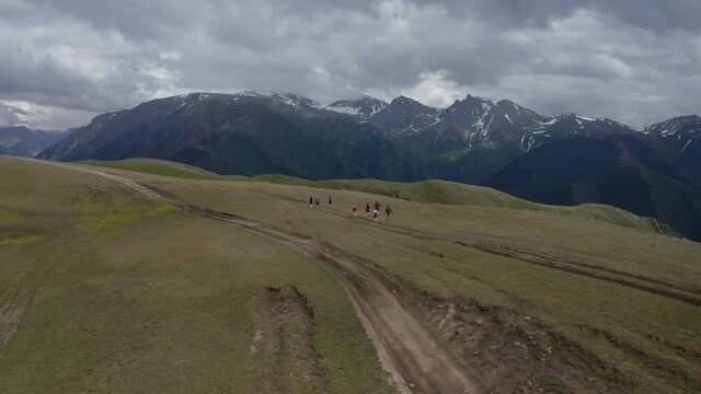 Aerial flight over group of people running in mountain plateau. Kazakhstan